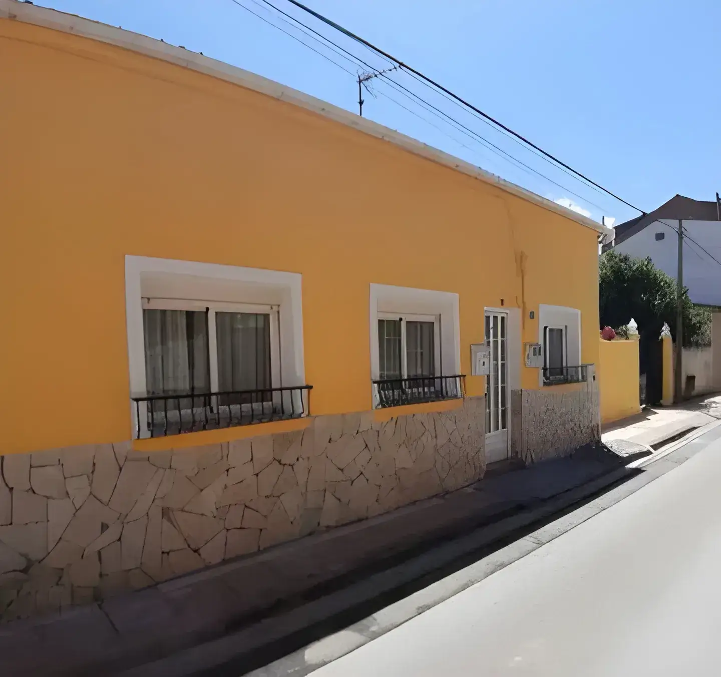 Los Pintores en Málaga Fachada de casa tradicional pintada en color amarillo con zócalo de piedra